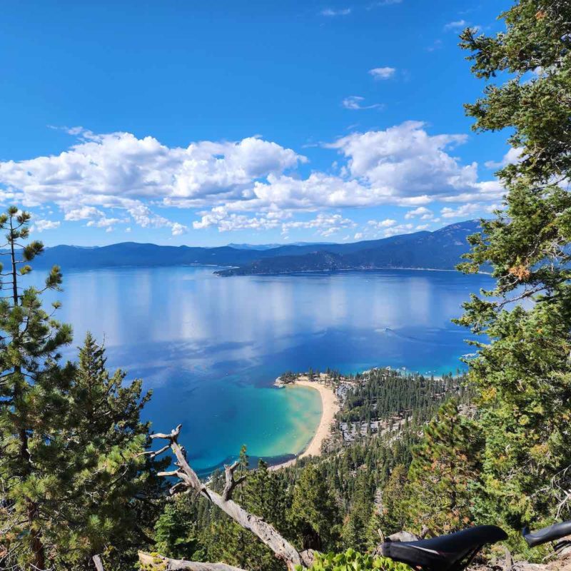 bikerumor pic of the day a photo of a view out over a clear blue lake with the seat of a bicycle in the bottom right corner, the sky is blue and had fluffy white clouds on the horizon.