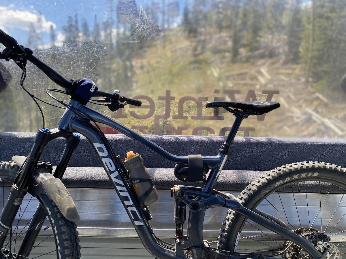 bikerumor pic of the day a mountain bike is by the window of a gondola riding up a ski mountain at winter park, the day is sunny and bright.