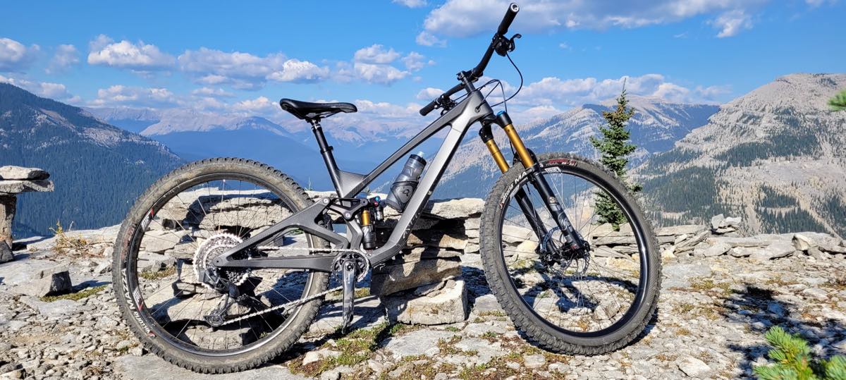 bikerumor pic of the day a mountain bike is on a rocky outcrop overlooking a mountain range, it is bright and sunny and there are fluffy white clouds in the sky.