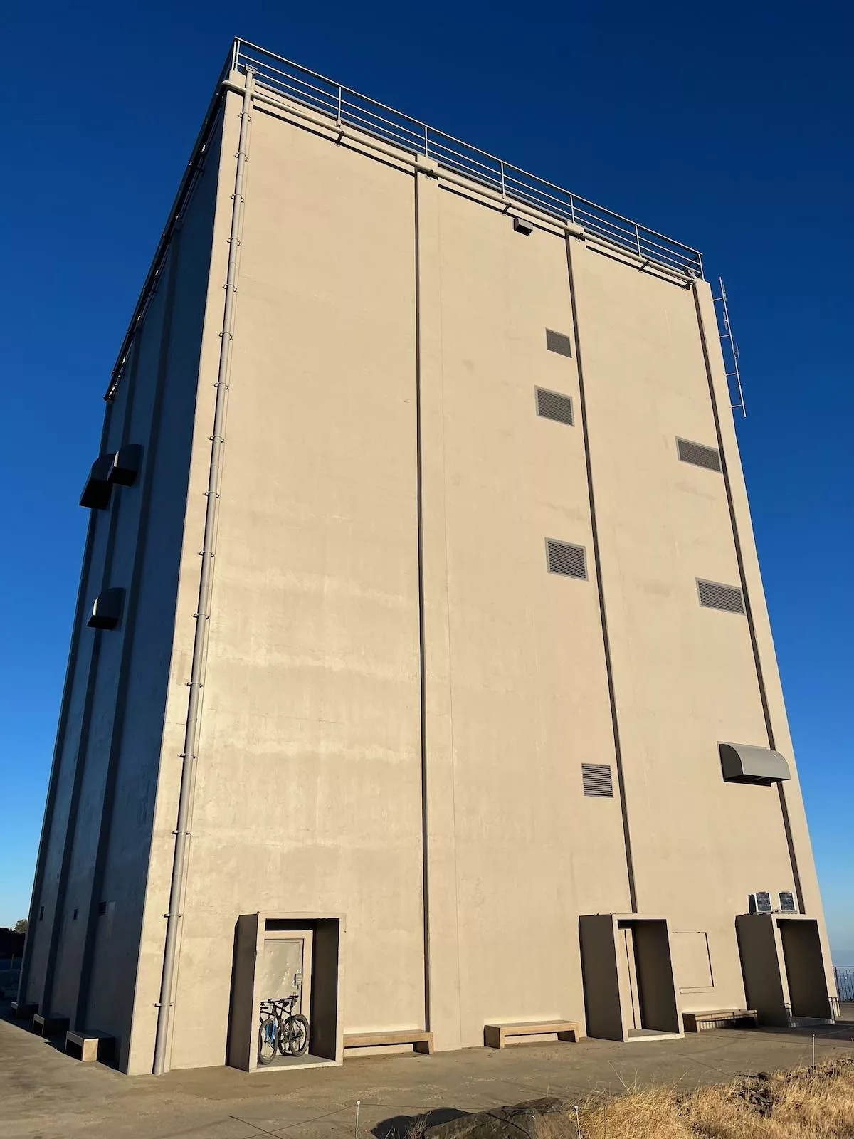 bikerumor pic of the day a bicycle is in the doorway of a large radar tower box like structure made of concrete, the sun is shining on that side of the box and the sky is surrounding it in dark blue.