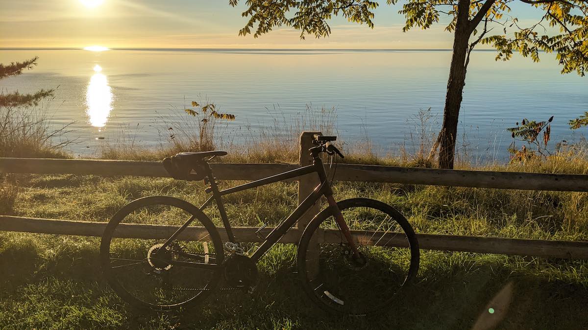 bikerumor pic of the day a bicycle leans against a wood split fence with a large lake a few meters away and a sunrise just at the edge across the lake