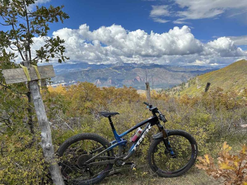 bikerumor pic of the day a mountain bike leans against a wood trail sign with brush and mountains in the distance and fluffy white clouds on the horizon