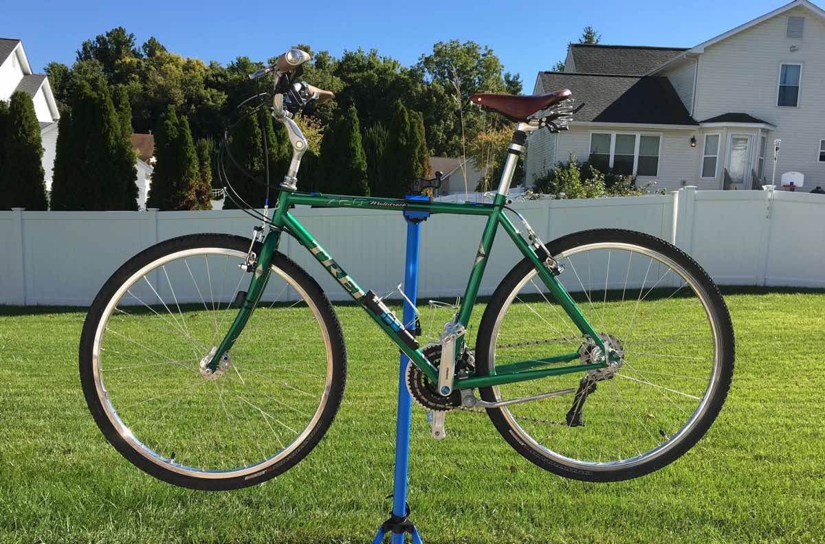 bikerumor pic of the day a trek bicycle is on a stand in a yard covered in short green grass surrounded by a white fence, there are houses and trees beyond the fence, the day is sunny and clear.