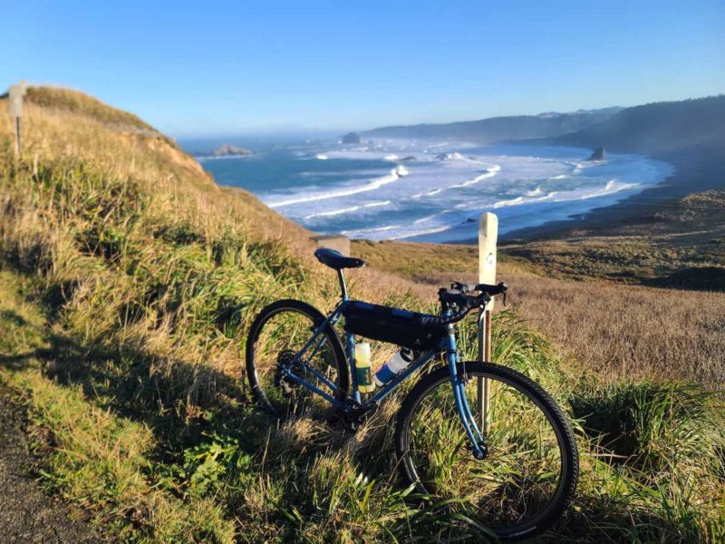 bikerumor pic of the day a bicycle leans against a marker on a hillside of grasses overlooking a bay as ocean waves are coming in