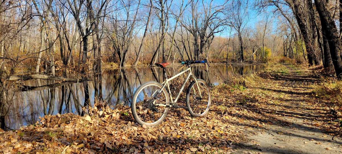 bikerumor pic of the day a bicycle on a path next to a stream it is fall and the sun is bright and all the leaves have fallen on the ground