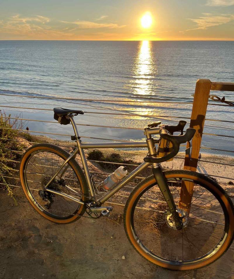 bikerumor pic of the day a bicycle leans against a cable fence along the beach as the sun sets over the water.