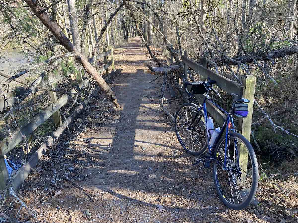 bikerumor pic of the day a bicycle leans against a bridge on a dirt path surrounded by trees whose leaves have fallen, one tree has broken across the bridge