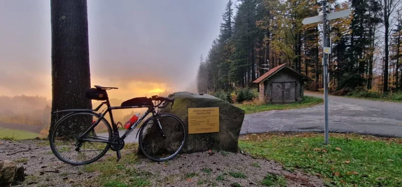 bikerumor pic of the day a bicycle leans against a large boulder at the top of a mountain with the sunset in the distance and a forest to one side.