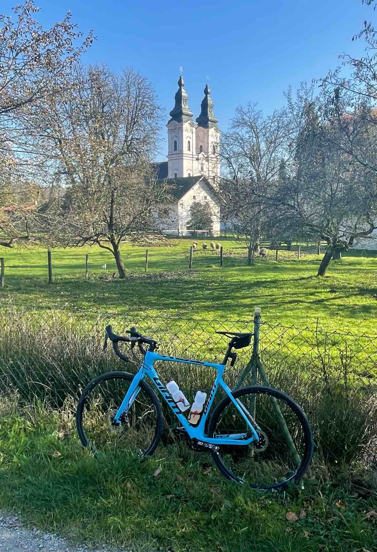 bikerumor pic of the day a bicycle leans against a wire fence surrounding a grassy field with sheep grazing and an abbey in the distance.