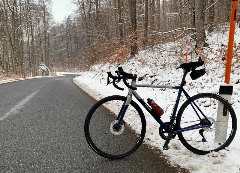 bikerumor pic of the day a road bike leans against a pole on the side of a road, there is snow on the ground around road