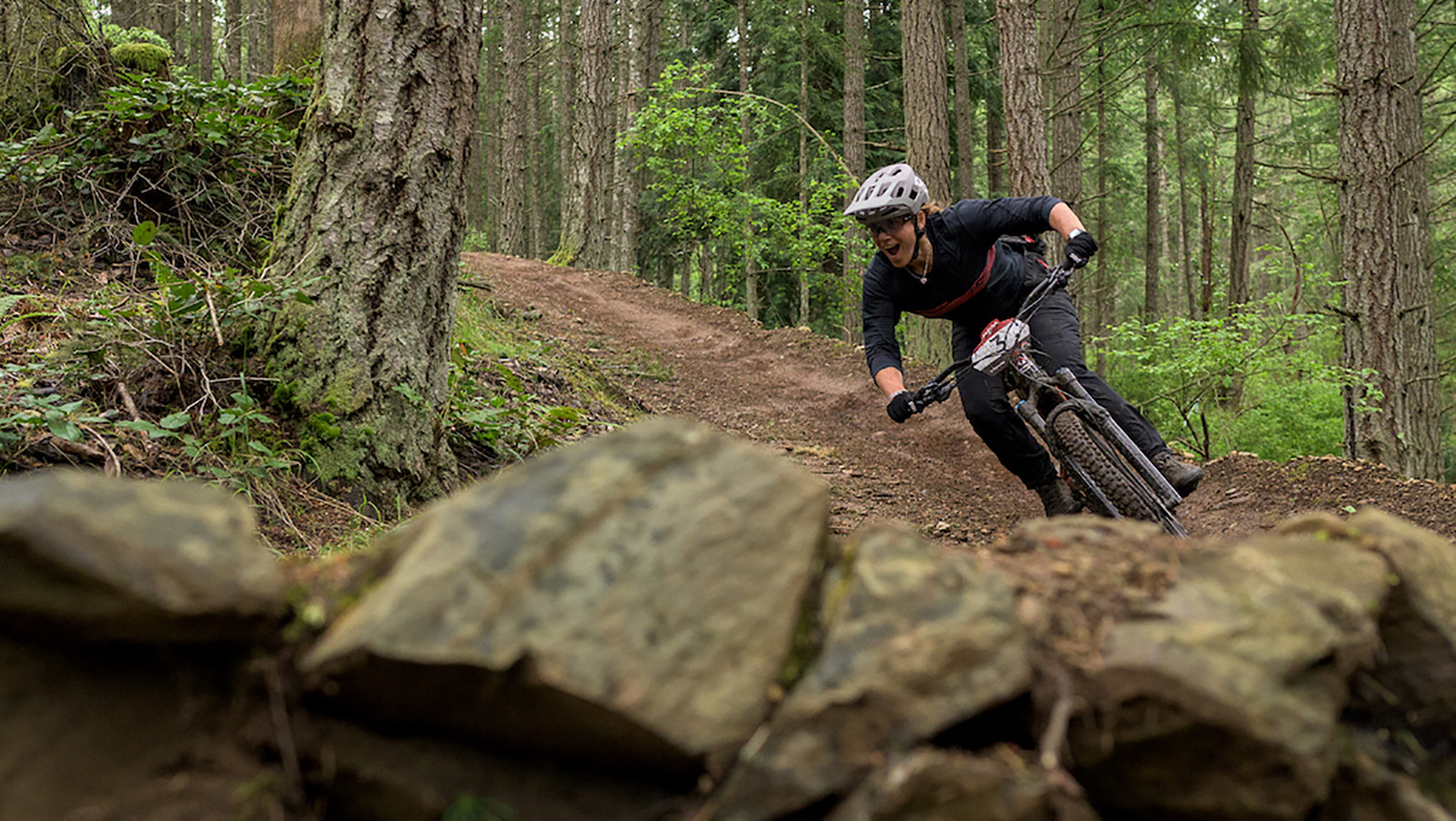 a rider takes a banked turn on a forested trail