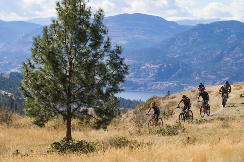 a group of riders riding eMTB on a trail above a lake