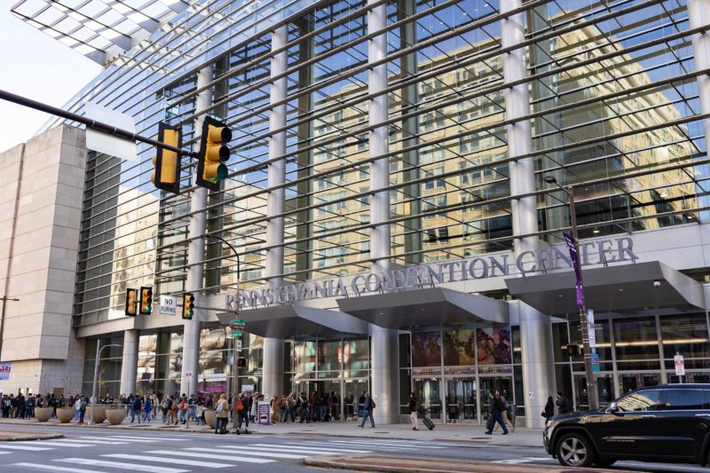 a medium wide view of a glassed convention center with people walking on the sidewalk in front of it