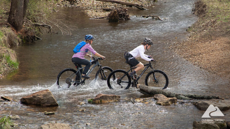 walmart ozark trail mountain bikes being ridden through a stream