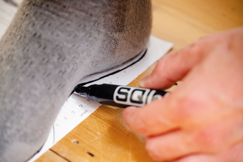 A man draws a line around his foot using the SQlab home measurement kit.