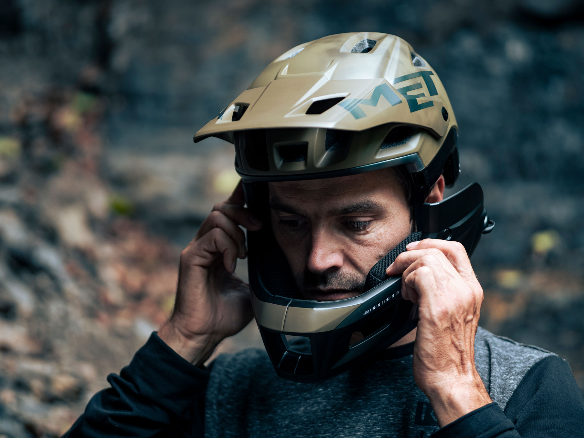 A man removing the chin bar from a Mete Parachute helmet in a wooded environment.