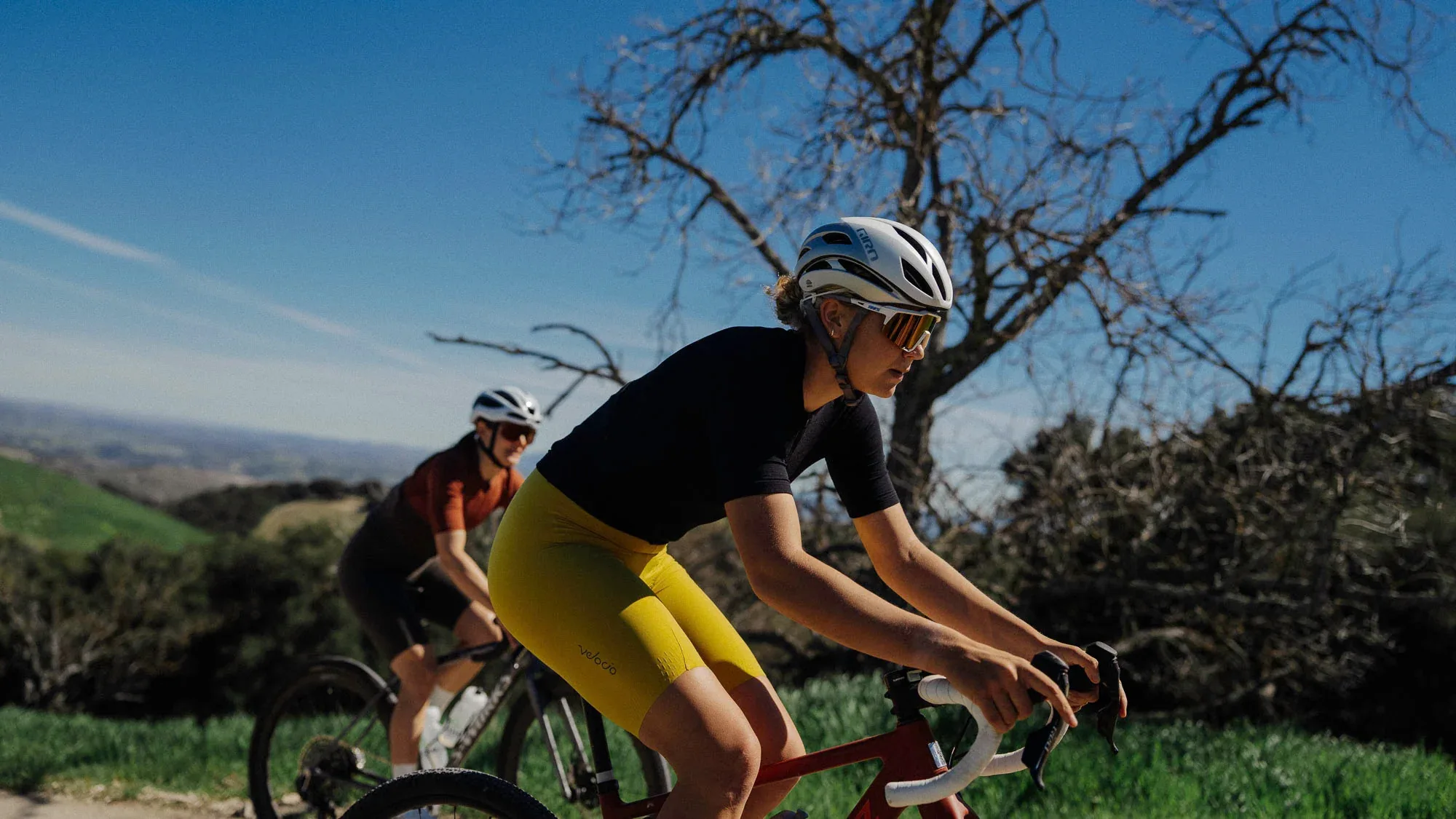 Two women climb under sunny skies, wearing Velocio Luxe apparel. 