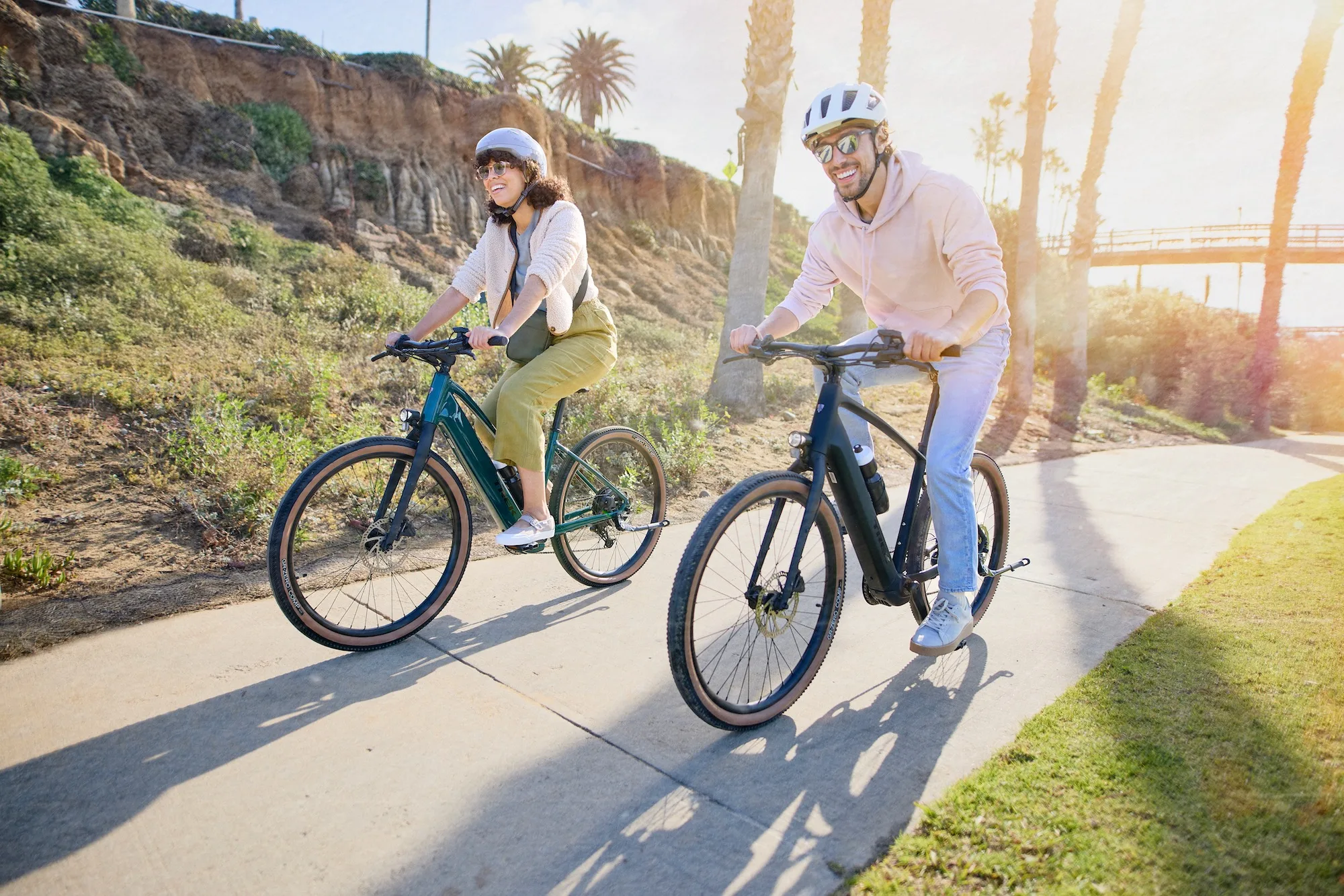 two riders on the Trek FX+1 e-bikes, smiling while riding on a paved path