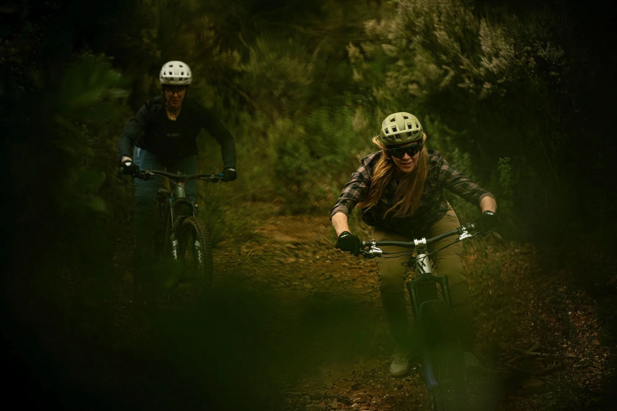 Two female riders riding mountain bikes while wearing the MET Shelter MIPS