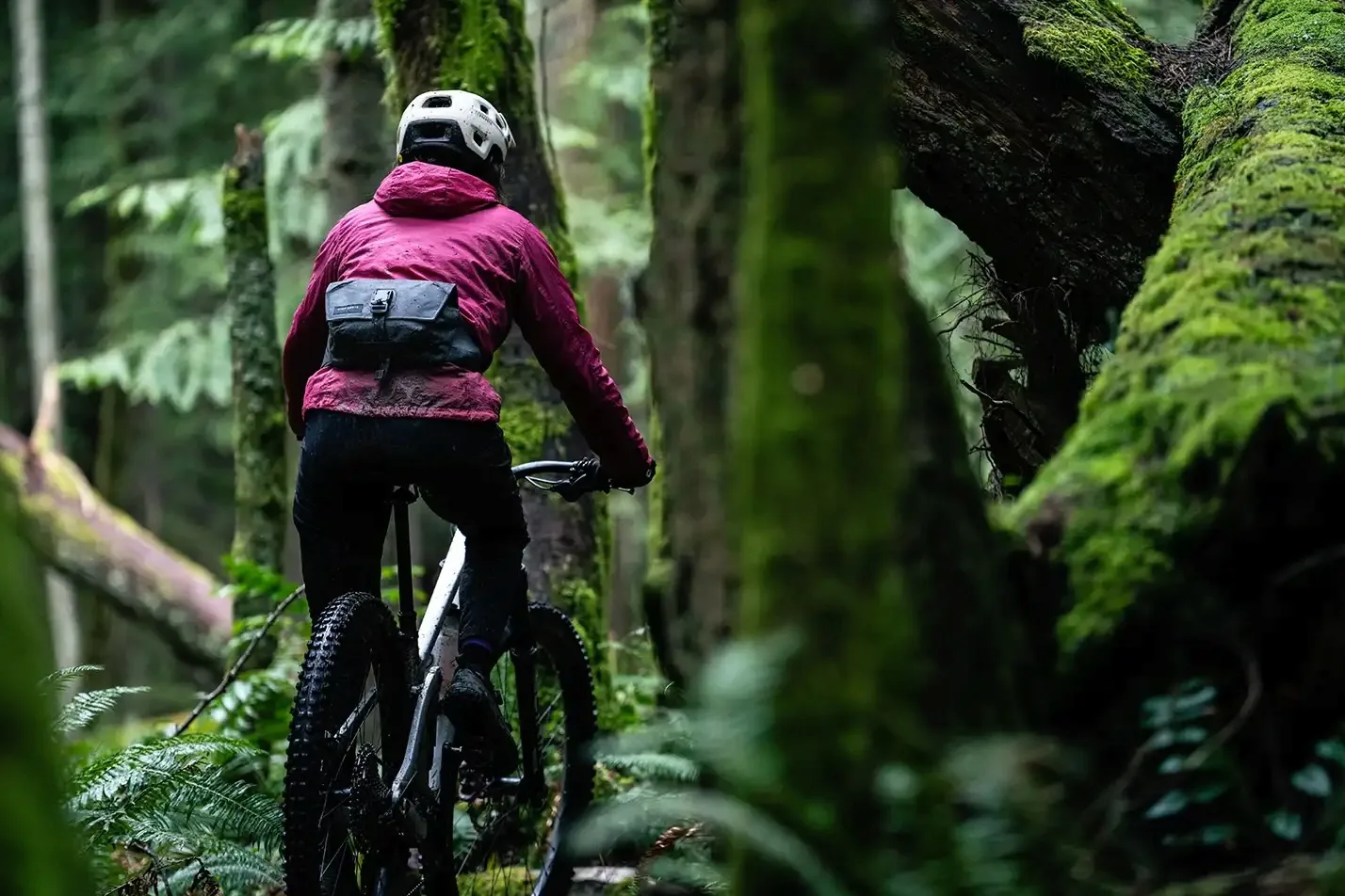 A female rider wearing the High Above Venture 3D hip pack while riding through the forest.