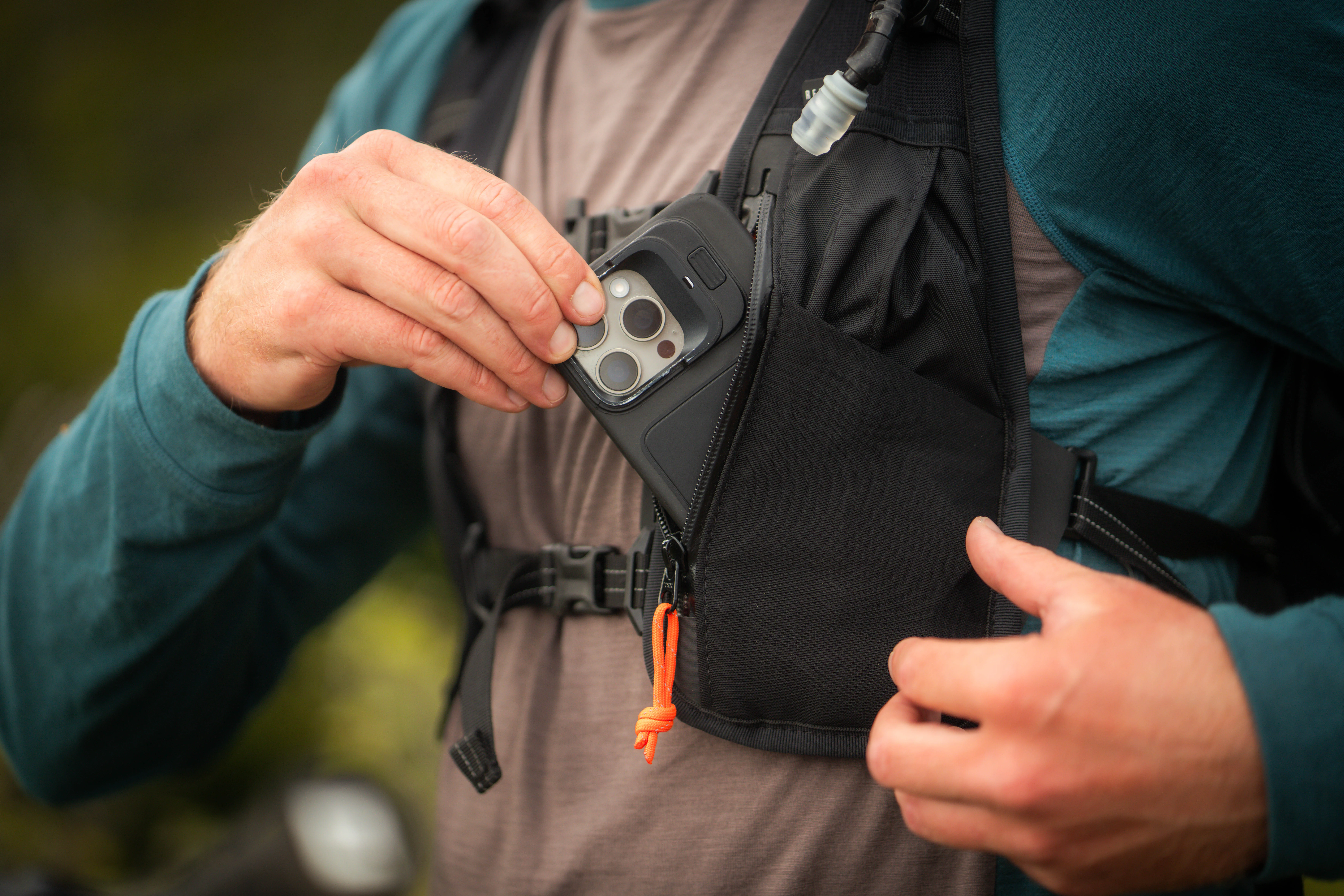 A rider putting their phone in the left zipper pocket on the Restrap Rolltop Hydration Vest
