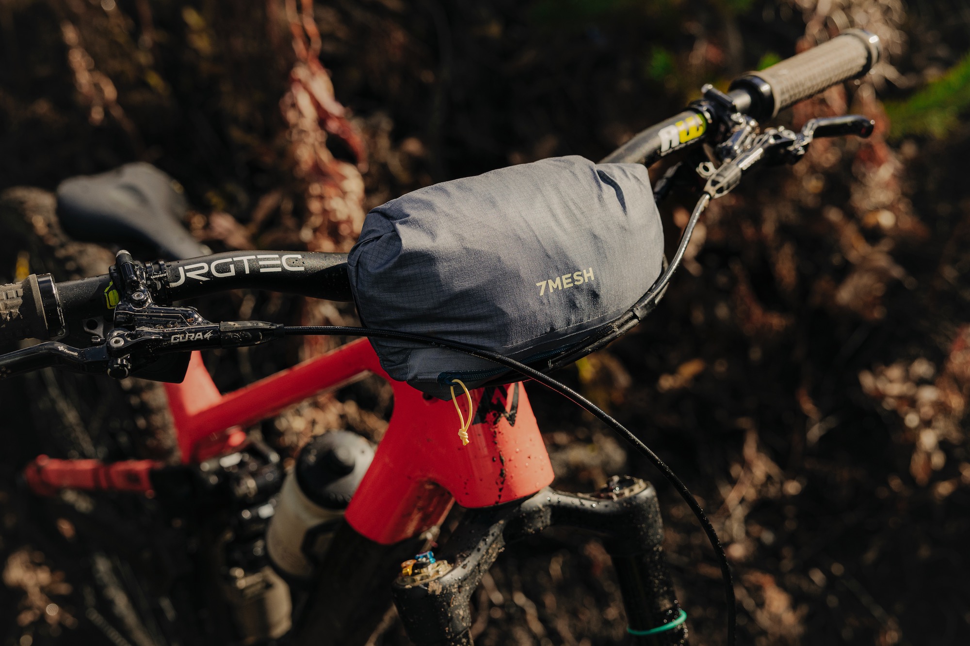 The 7Mesh Guardian Jacket packed into its own pocket and stashed on the handlebar of a mountain bike.