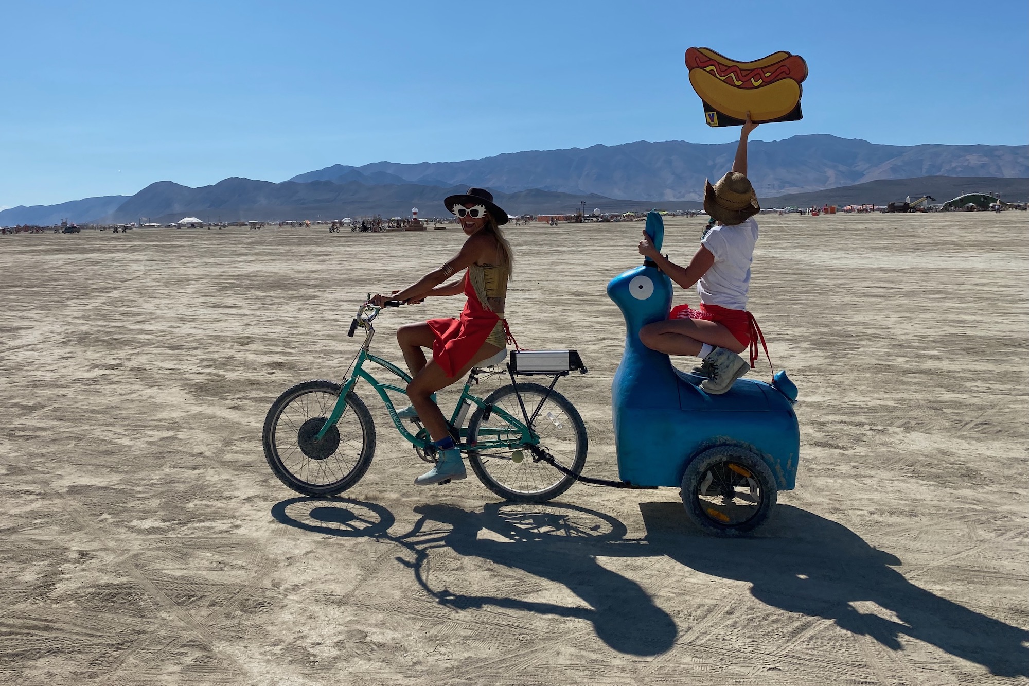 A woman riding a bike while towing a small trailer with a passenger on it.