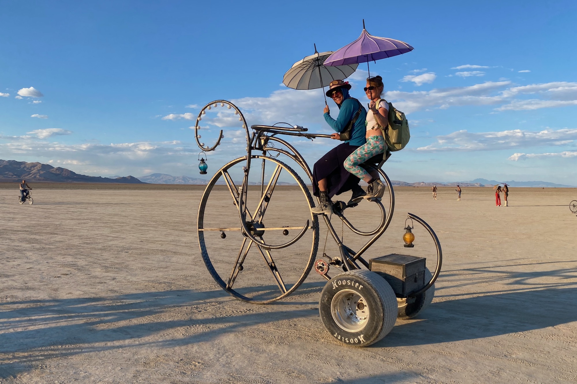 Randy riding his crazy trike bike at burning man with a passenger on the back.