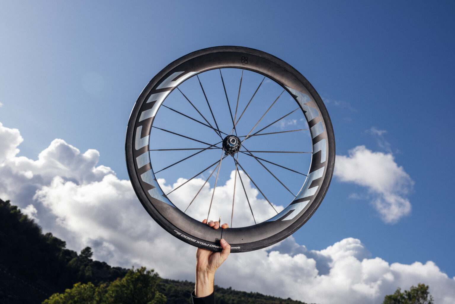someone holding up the Miche Deva RD wheel with a blue sky in the background