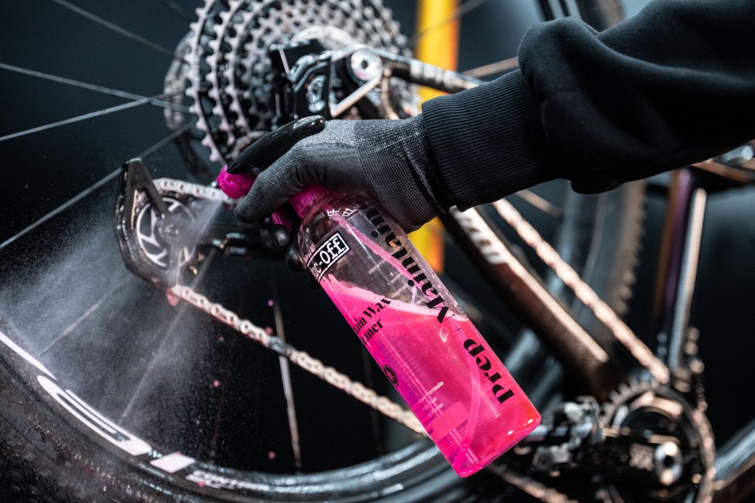 a mechanic spraying Muc-Off Chain Wax Cleaner on a chain