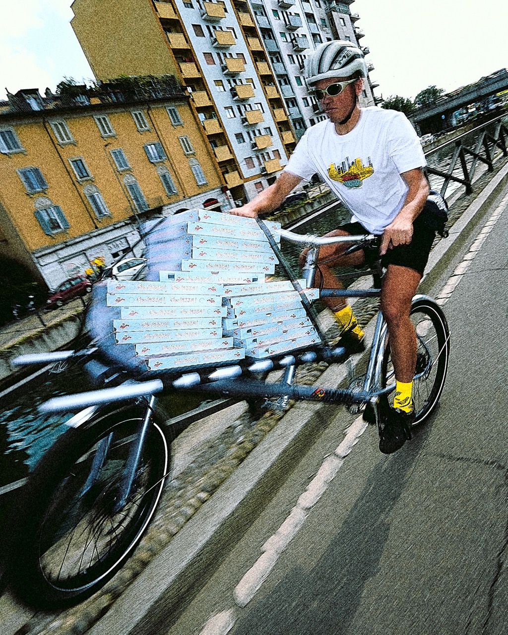 A rider with lots of pizza cargo on the front rack of the OMNIUM x Cinelli Supercargo bike riding a wheelie through the city streets