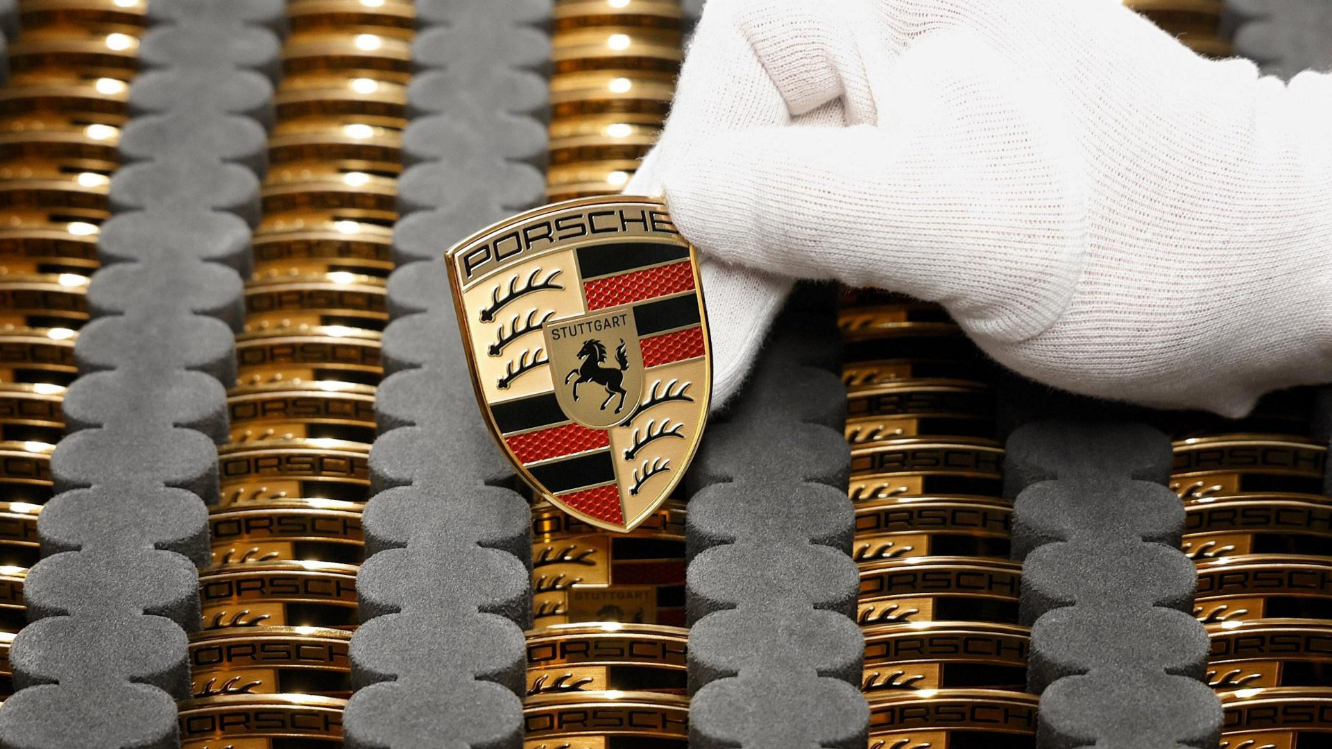 gloved hand holding a porsche head badge.