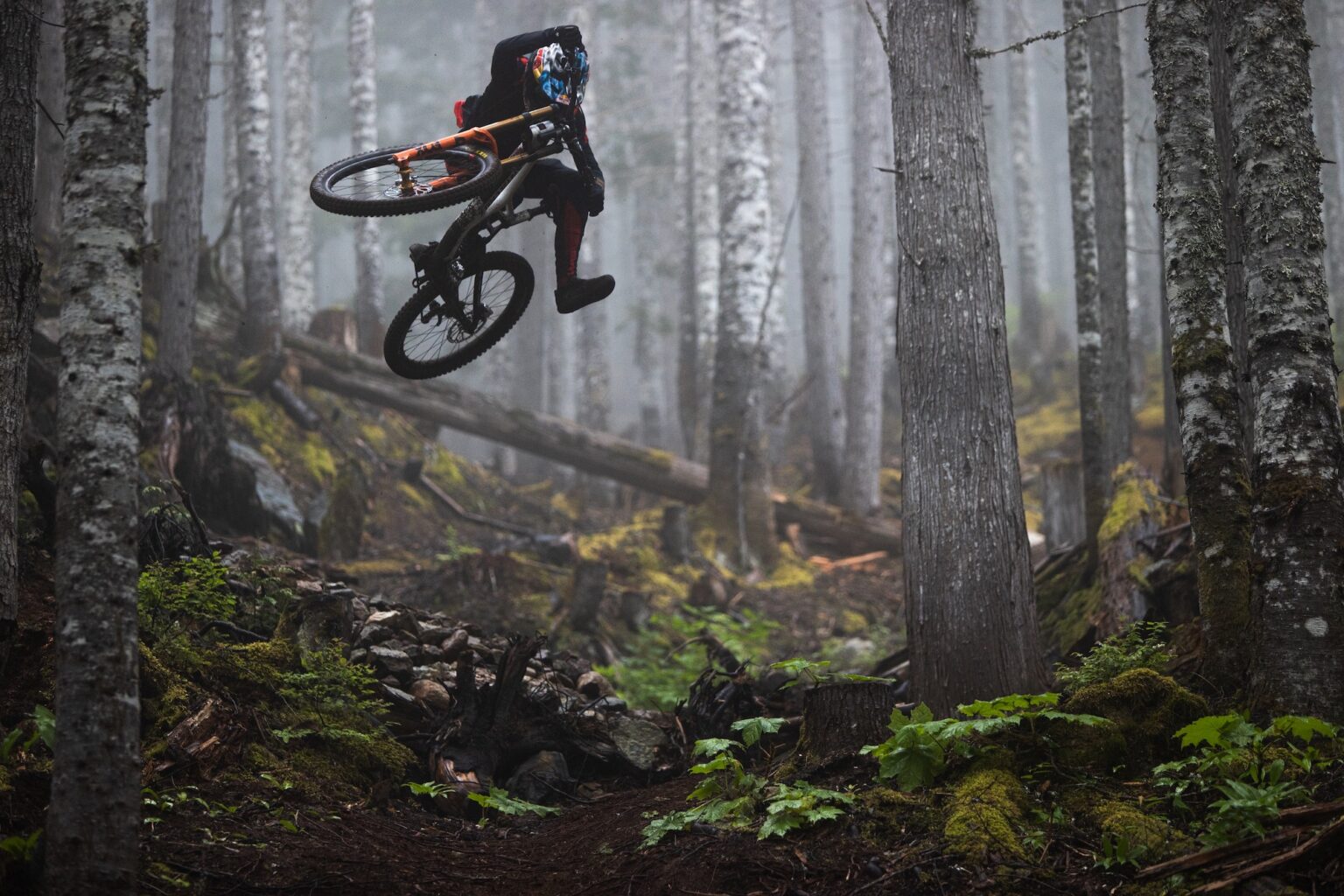 Jackson Goldstone kitting a jump on his downhill bike in the forest.