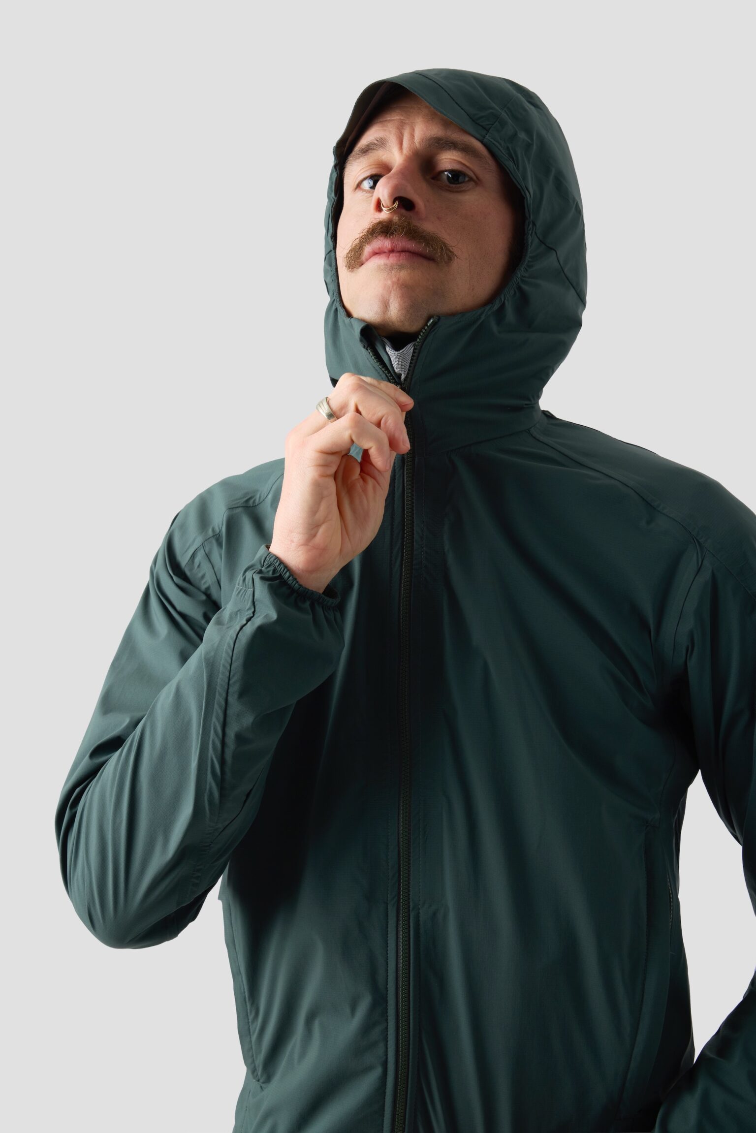 studio image of a man wearing the Ornot Fog eater Hooded Rain Jacket zipping the hood up