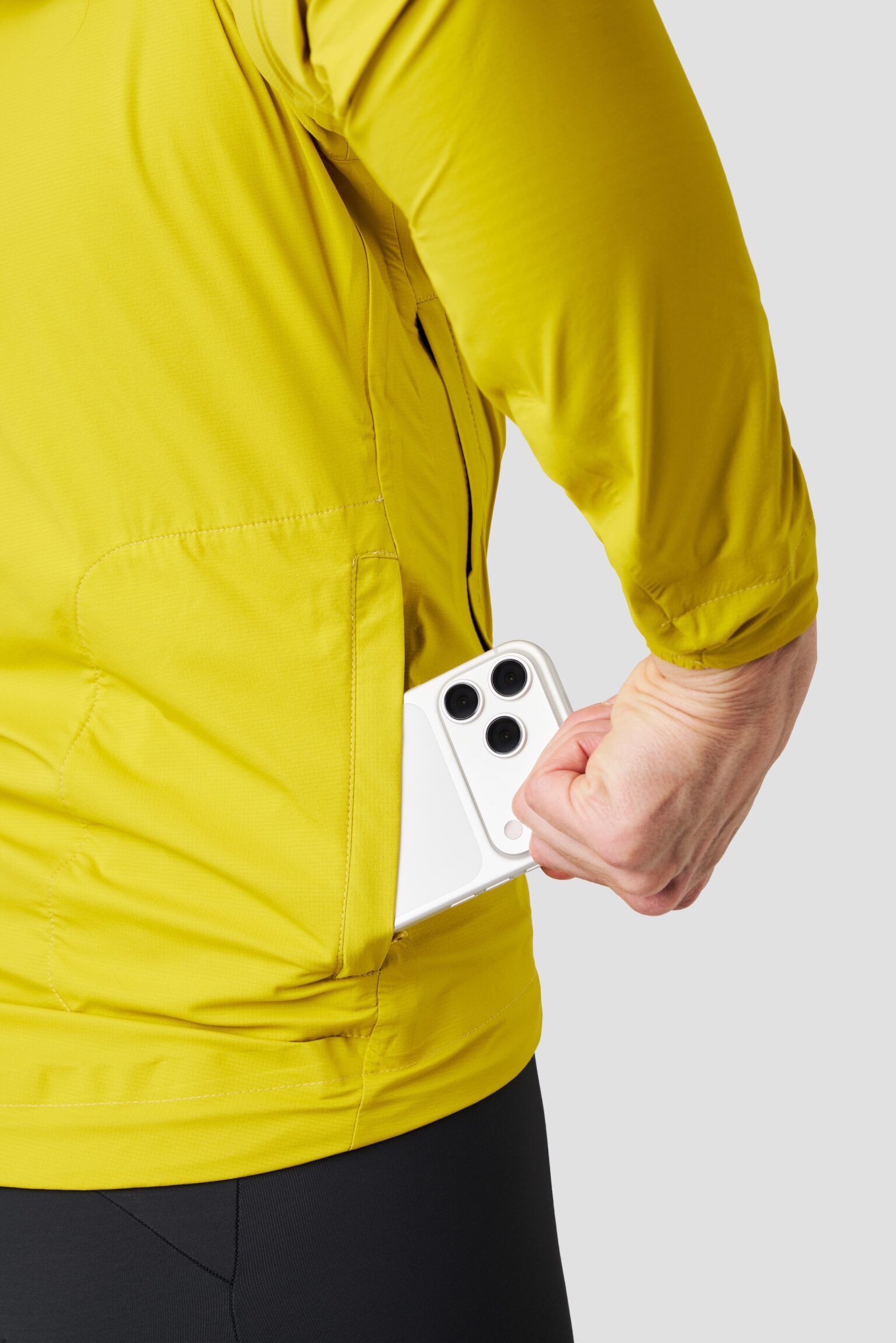 studio image of a woman wearing the Ornot Fog eater Hooded Rain Jacket using the back pocket