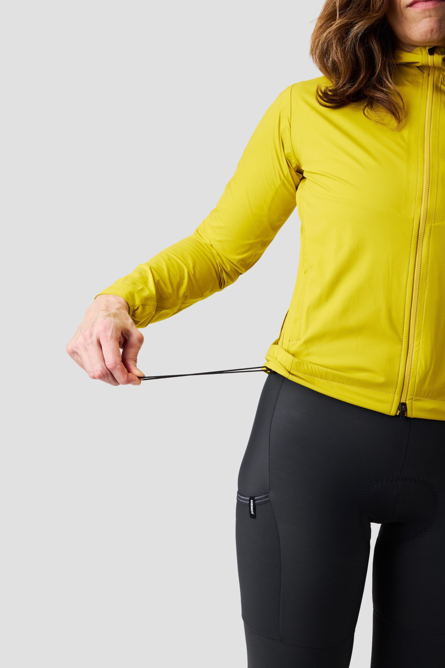 studio image of a woman wearing the Ornot Fog eater Hooded Rain Jacket pulling the drawcord hem