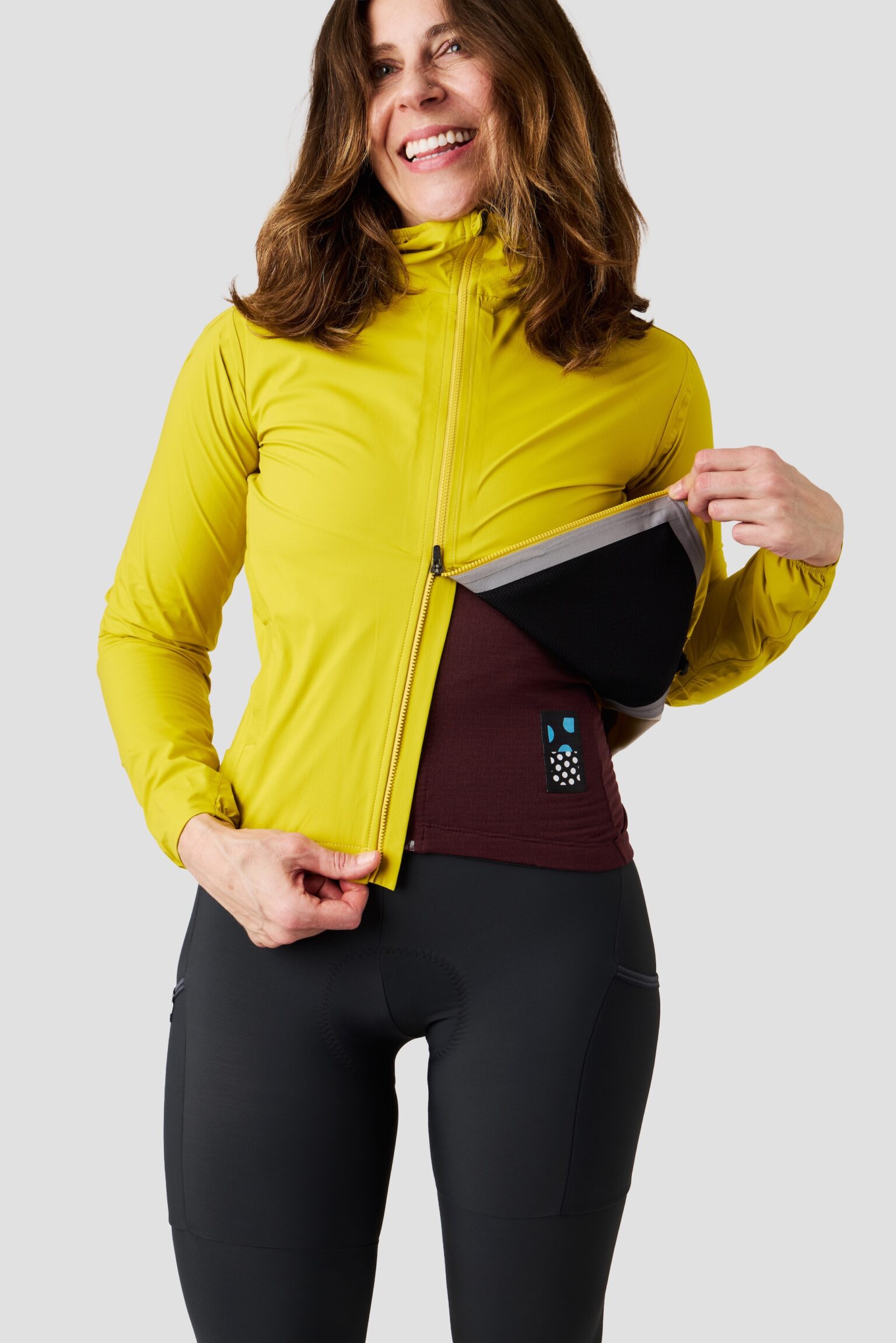 studio image of a woman wearing the Ornot Fog eater Hooded Rain Jacket using the 2-way zipper